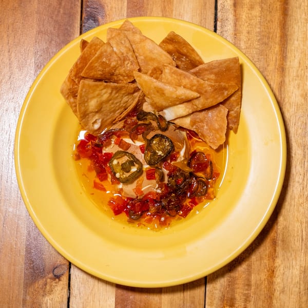 A yellow plate of crispy tortilla chips with a creamy dip topped with jalapeños and red peppers.