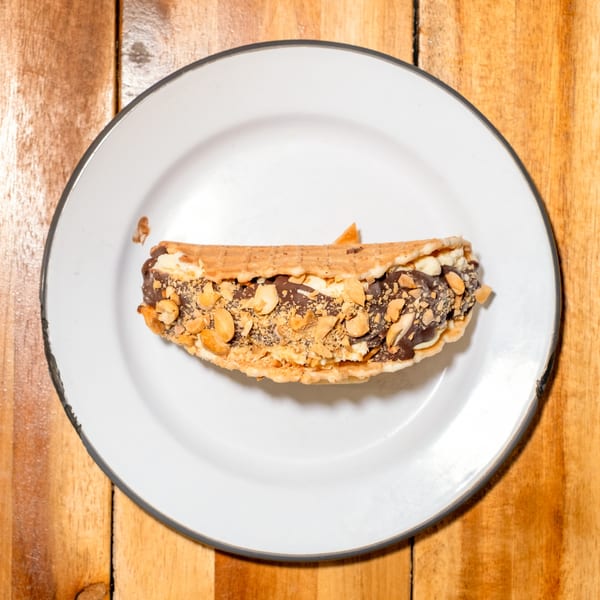 Waffle taco filled with chocolate, ice cream, and peanuts on a white plate.