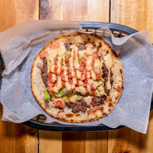 A flatbread pizza with ground meat, lettuce, diced tomatoes, and a creamy sauce in a basket.