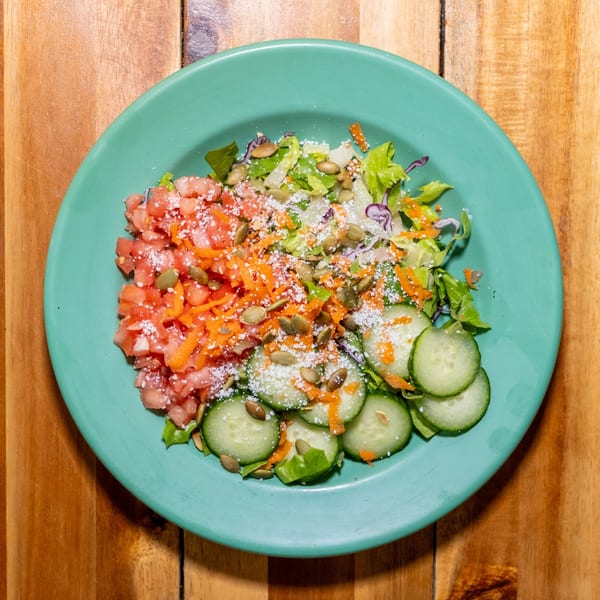 A vibrant salad with diced tomatoes, shredded carrots, sliced cucumbers, lettuce, and pumpkin seeds.