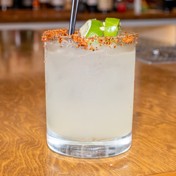 A refreshing margarita with a chili-lime rim and lime wedges, served on a wooden table.