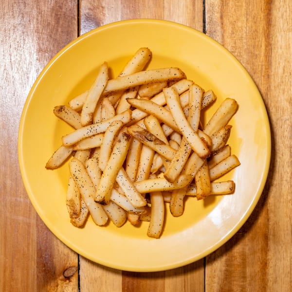 Golden french fries seasoned with pepper on a bright yellow plate, on a wooden table.